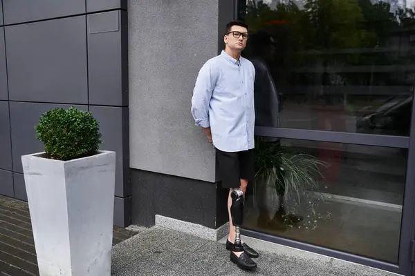 Handsome young man stands next to a window, proudly displaying his prosthetic leg in casual attire. — Stock Photo