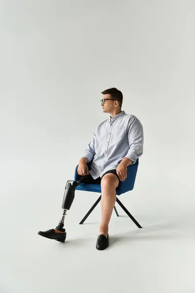 Handsome young man wearing glasses and a prosthetic leg sits in a contemporary chair. — Stock Photo