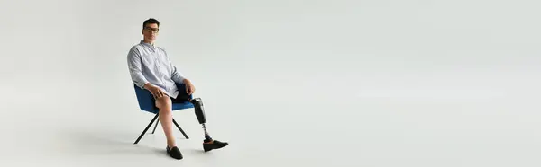 A young handsome man sits relaxed in a chair, showcasing his prosthetic leg with pride in a studio. — Stock Photo