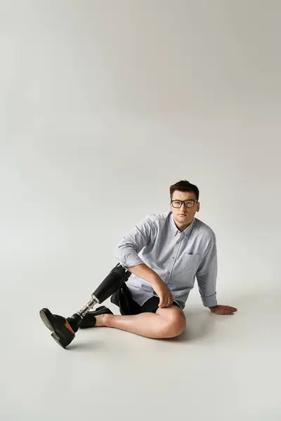 Young man relaxes on the floor, highlighting his stylish prosthetic leg in a simple background. — Stock Photo