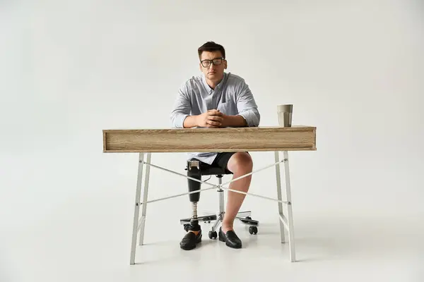 Joven guapo se sienta con confianza en un escritorio minimalista, mostrando su pierna protésica. - foto de stock