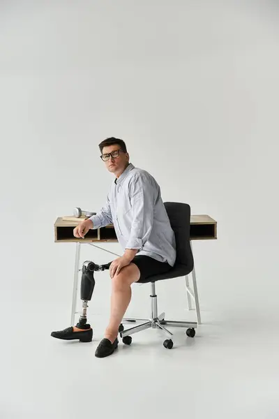 Man with a prosthetic leg sits confidently at a modern desk, dressed casually in a button up shirt. — Stock Photo