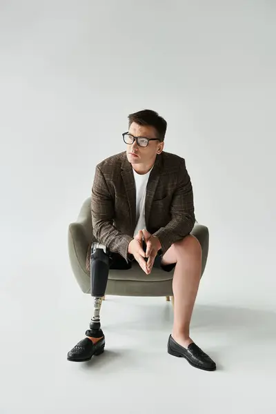 Man with a prosthetic leg is sitting thoughtfully in a modern chair, dressed stylishly. — Stock Photo