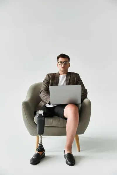 Handsome young man with prosthetic leg focuses on laptop while relaxing in chair — Stock Photo