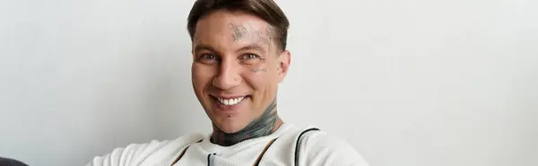 Ein junger Mann mit Tätowierungen lächelt strahlend in einem gut beleuchteten Innenbereich. — Stockfoto