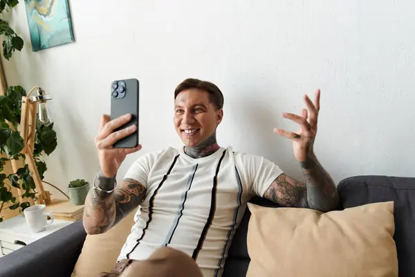 Un joven guapo con tatuajes disfruta de una conversación en su smartphone en casa. — Stock Photo