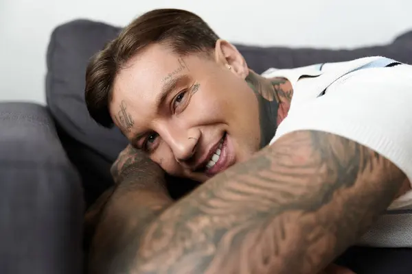 Young man with tattoos relaxes on a couch, showcasing a bright smile and engaging demeanor. — Stock Photo