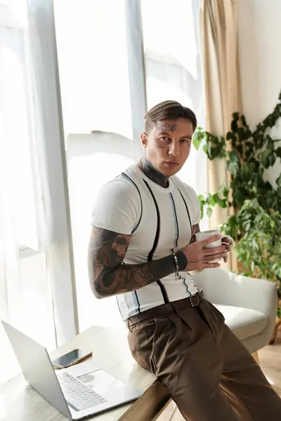 Tattooed young man relaxes in a stylish workspace, sipping a cup and enjoying the moment. — Stock Photo