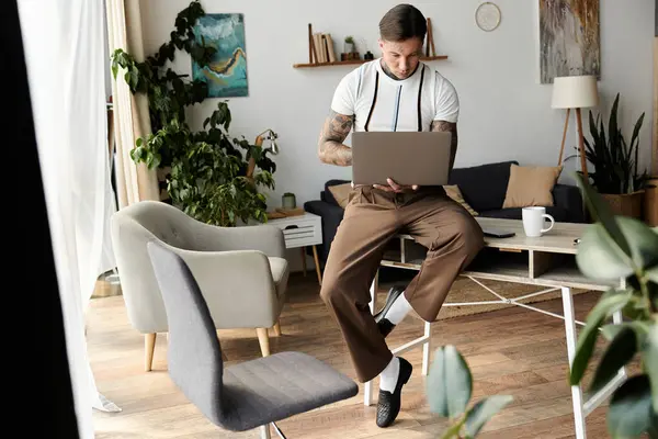 Handsome young man with tattoos engages with laptop in stylish living room filled with plants. — Stock Photo