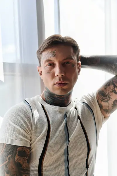 Young man with tattoos showcases his style and confidence in a well lit indoor space. — Stock Photo