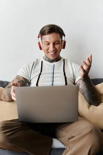 A young handsome man with tattoos is smiling and engaging in a virtual chat while seated. — Stock Photo