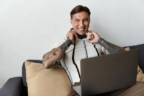 Smiling young man with tattoos listens to music on headphones while using a laptop. — Photo de stock