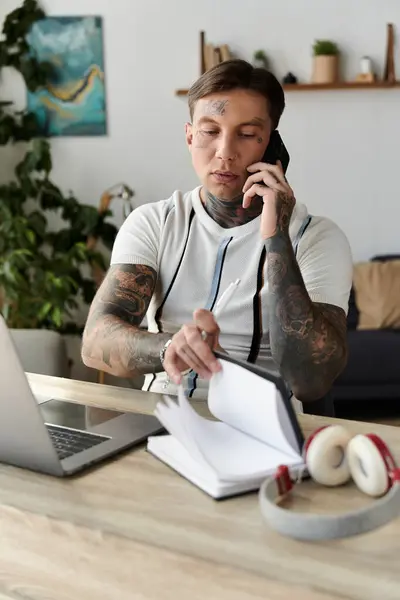 Handsome young man with tattoos talks on the phone while writing in a notebook. - foto de stock