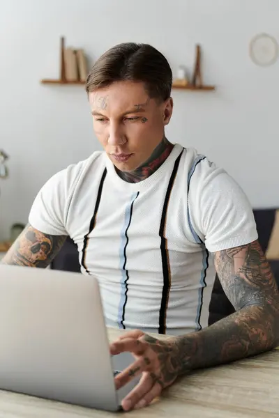 Joven hombre guapo con tatuajes trabaja intensamente en su computadora portátil en un escritorio elegante - foto de stock
