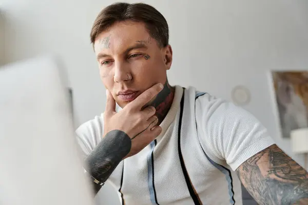 Молодий чоловік з татуюваннями концентрується, використовуючи свій ноутбук у світлій кімнаті. — стокове фото
