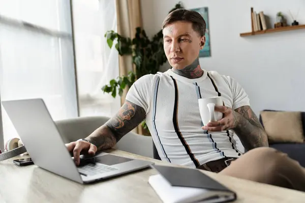 Handsome young man with tattoos focused on his laptop in a stylish and inviting room — Stock Photo