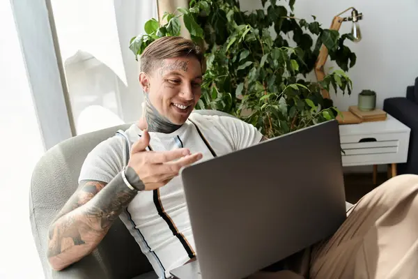 Un giovane uomo con tatuaggi sorride e gesti mentre è impegnato in una videochiamata nel suo accogliente salotto. — Foto stock