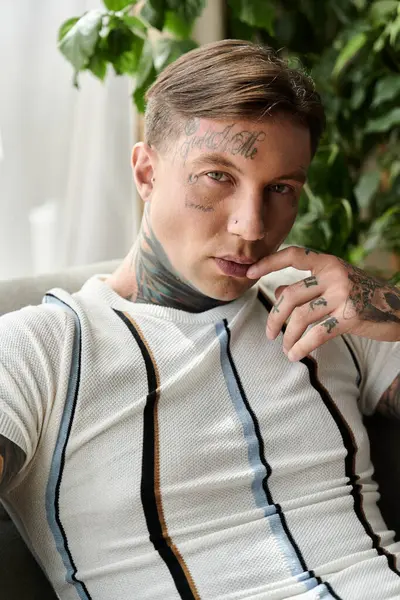 A young man with notable tattoos relaxes in a cozy indoor setting, exuding confidence. — Stock Photo