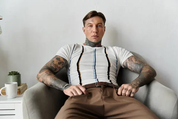A young man with tattoos sits confidently in a cozy chair, showcasing his style and demeanor. — Stock Photo