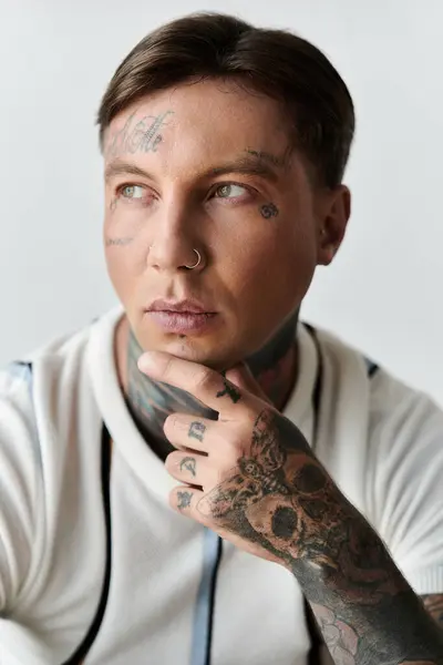 A young man with tattoos sits quietly, his hand on his chin, reflecting deeply in a bright space. — Stock Photo