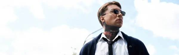 A young handsome man with tattoos poses outdoors wearing sunglasses and a smart outfit. — Stock Photo