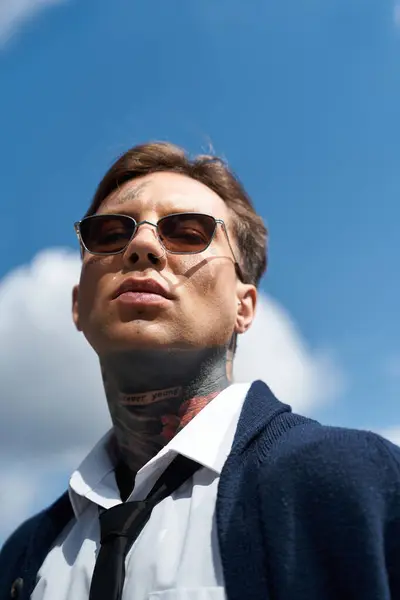 Handsome young man with tattoos and sunglasses poses confidently against a clear sky. — Photo de stock