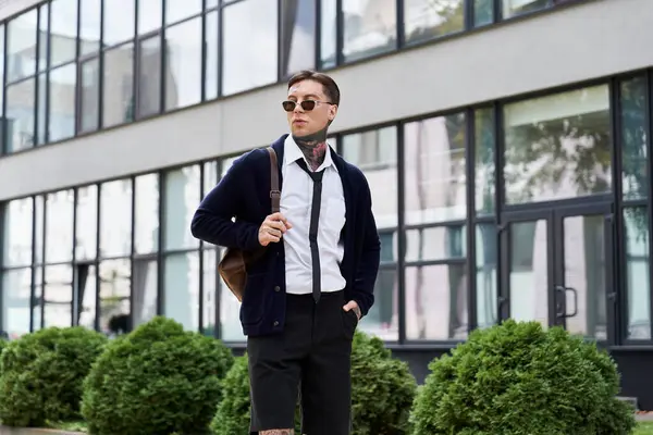 Tattooed young man in stylish attire strolls happily by a modern building. — Stock Photo