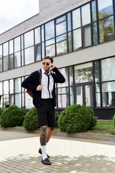 Bel giovanotto tatuato passeggia fiducioso vicino a una struttura contemporanea alla luce del giorno. — Foto stock