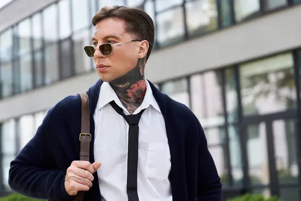 Young man with tattoos and stylish outfit strolls by modern buildings on bright day. — Stock Photo