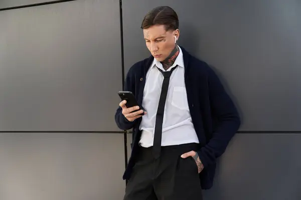 Стильный молодой человек с татуировками смотрит в телефон, одетый в формальный костюм и наклоняющийся. — стоковое фото