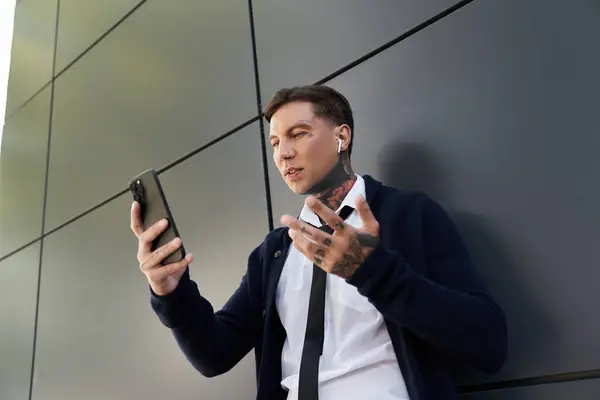 Handsome young man with tattoos talks on his smartphone while leaning against a wall. — Stock Photo