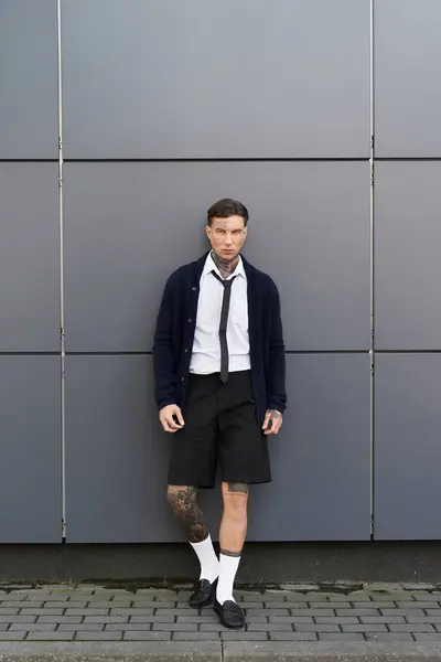 A young man with tattoos stands confidently in front of a contemporary building during daylight. — Stock Photo