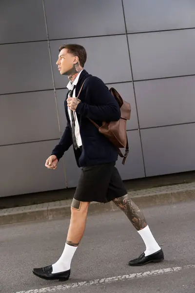 Handsome young man with tattoos strolls through a city area wearing a stylish outfit. — Stock Photo