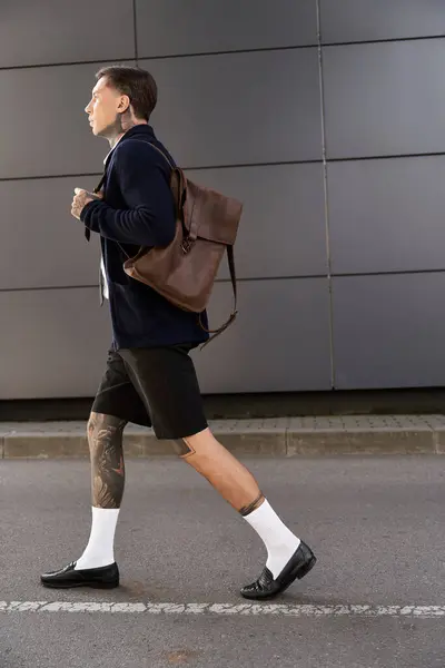 Handsome young man with tattoos strides confidently through a modern urban area. — Stock Photo