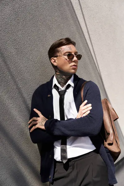 Handsome young man with tattoos stands with crossed arms, dressed smartly in an urban setting. — Stock Photo