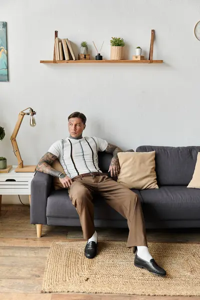 A young handsome man with tattoos sits comfortably on a sofa, enjoying a relaxed moment. — Stock Photo