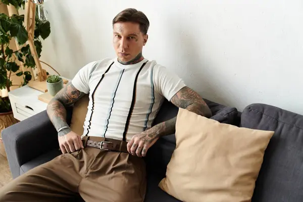 A young handsome man with tattoos relaxes on a couch in a contemporary interior setting. — Stock Photo