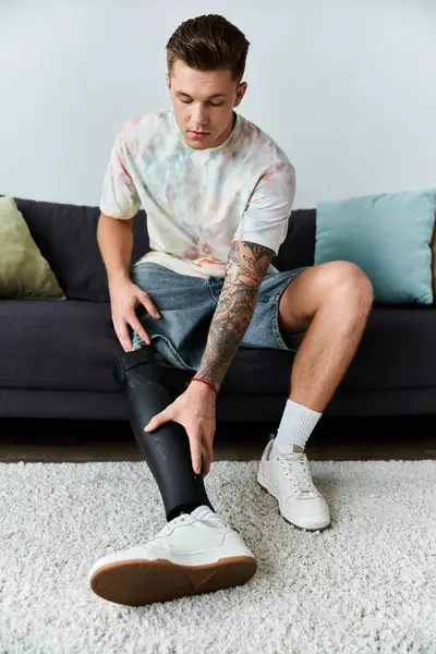 A young, handsome man sits on a couch, adjusting his sleek prosthetic leg with concentration. — Stock Photo