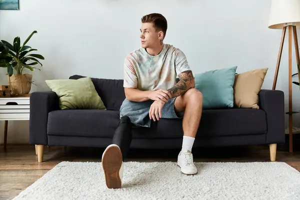 Um jovem com uma perna protética relaxa em um sofá elegante em uma sala brilhante e convidativa. — Fotografia de Stock