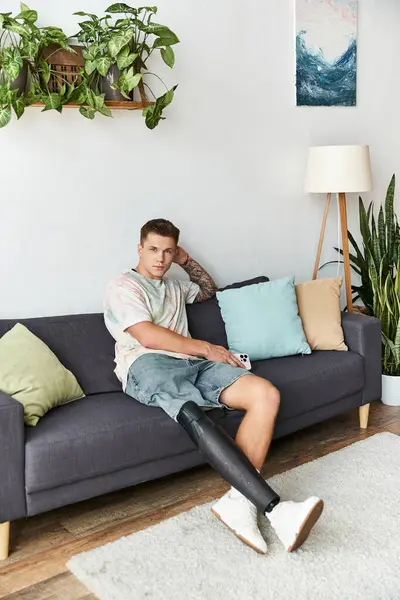 Handsome young man sitting comfortably on a couch, showcasing confidence with his prosthetic leg. — Stock Photo