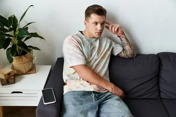 Handsome young man sits pensively on a modern couch surrounded by greenery. — Stock Photo