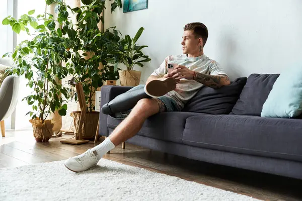 Beau jeune homme assis confortablement sur un canapé, profitant de son temps à l'intérieur tout en se relaxant. — Photo de stock