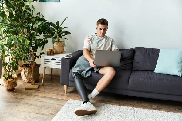 Young handsome man uses laptop on the couch in a bright and modern living room setting. — Stock Photo