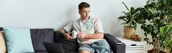 Handsome young man sits comfortably on a couch, enjoying his coffee. — Stock Photo