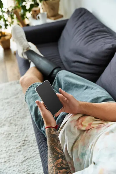 Handsome young man lounges comfortably on the sofa, holding his smartphone with ease. — Stock Photo
