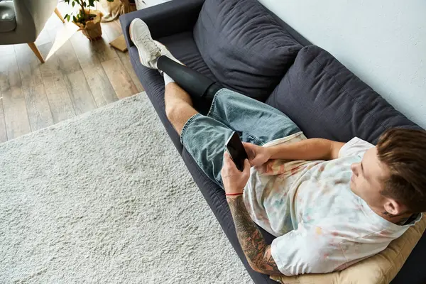 A young handsome man relaxes on a couch while using his phone, showcasing his vibrant personality. — Stock Photo