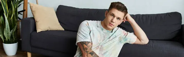 Handsome young man relaxes on a couch, showing off his tattooed arm with pride. — Stock Photo