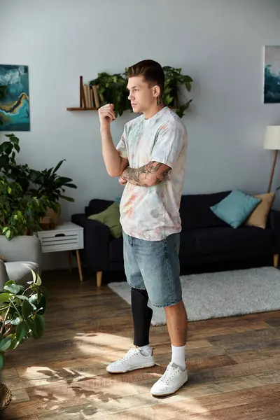 Handsome young man with a prosthetic leg stands in a modern living room, deep in thought. — Stock Photo