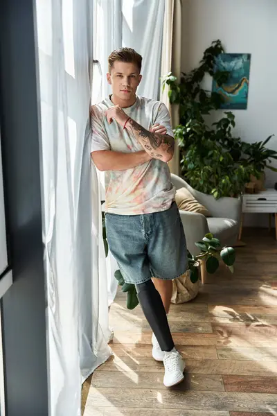 A confident young man with a prosthetic leg poses in sunlight among green plants. — Stock Photo