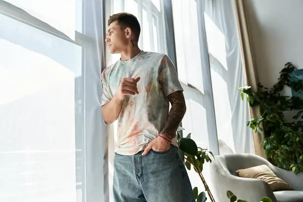 A young man stands by sunlight filled windows, contemplating life in style. — Stock Photo